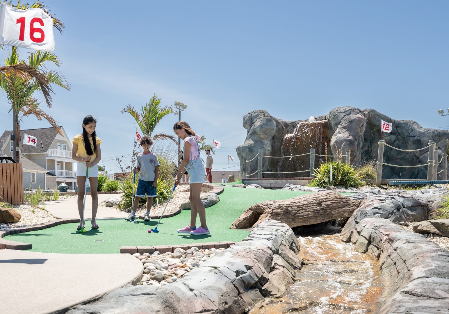 Three kids enjoy a round of miniature golf outside at Lighthouse Point at Jenkinson's Boardwalk