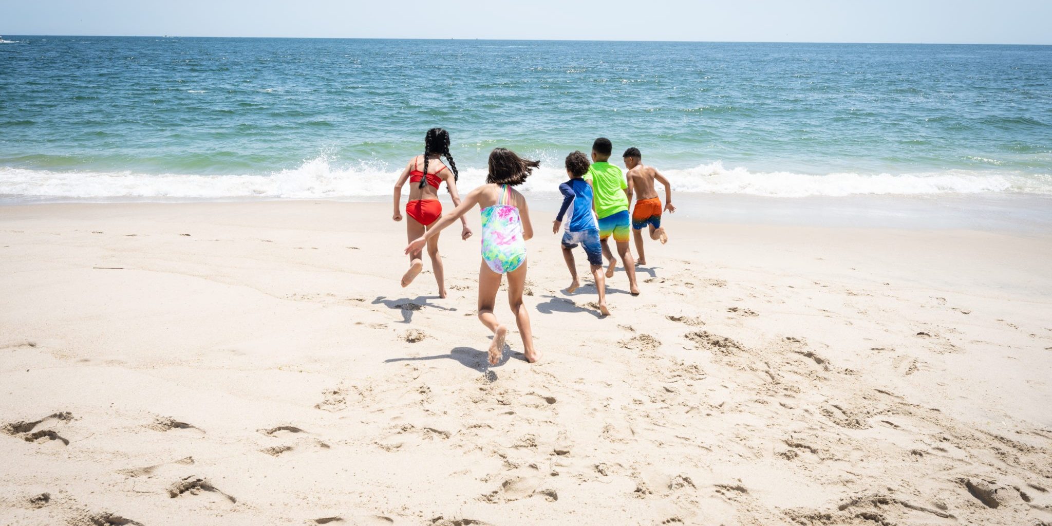 Five kids run toward the ocean in the sand at the beach located at Jenkinson's Boardwalk